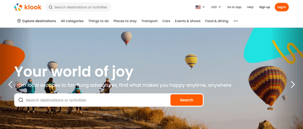 Klook homepage design with search bar over an image of cyclists on a hill with hot air balloons around them.